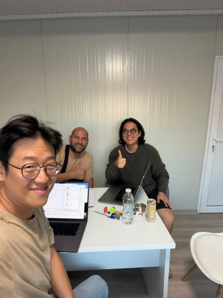Three people smiling at a white table with laptops open during a working session in an office in Bulgaria, two giving a thumbs-up.