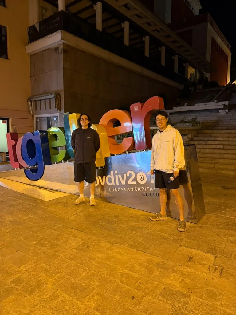 Two members of the LMN team standing at night beside the colorful 'together' letter sculpture in Plovdiv, Bulgaria.